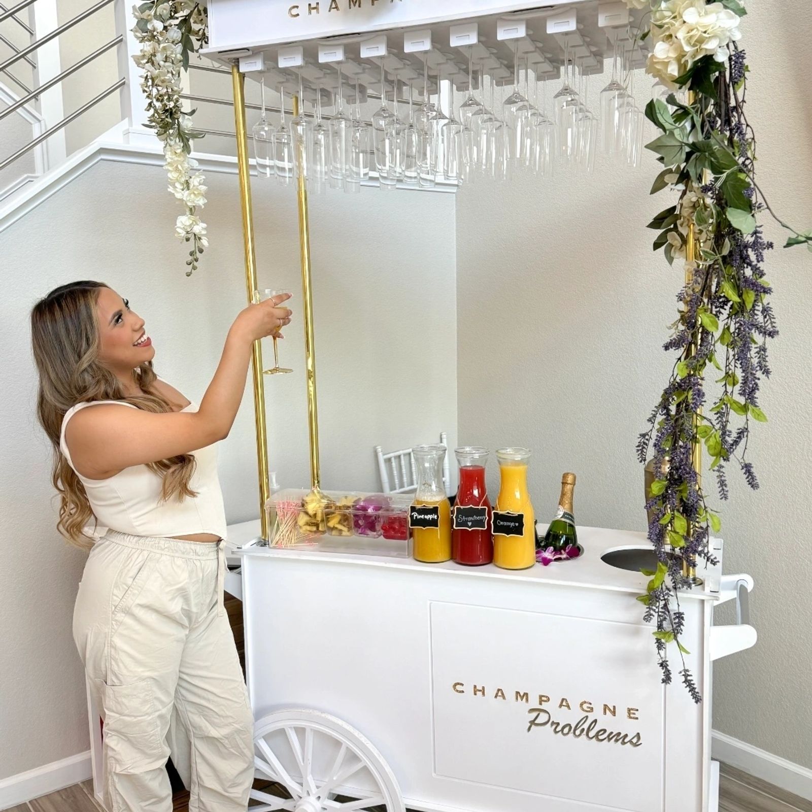 White bar cart with gold rails and greenery at an indoor celebration